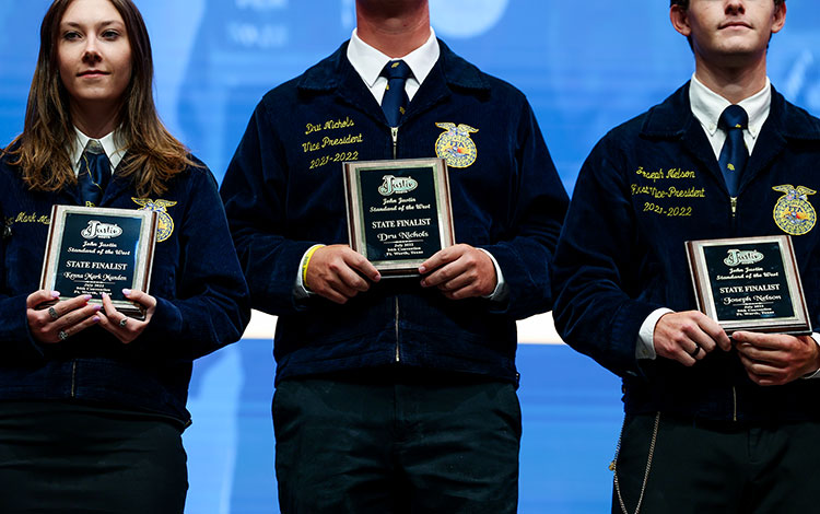 Three FFA members wearing blue corduroy jackets pose holding their plaques after receiving their FFA awards.